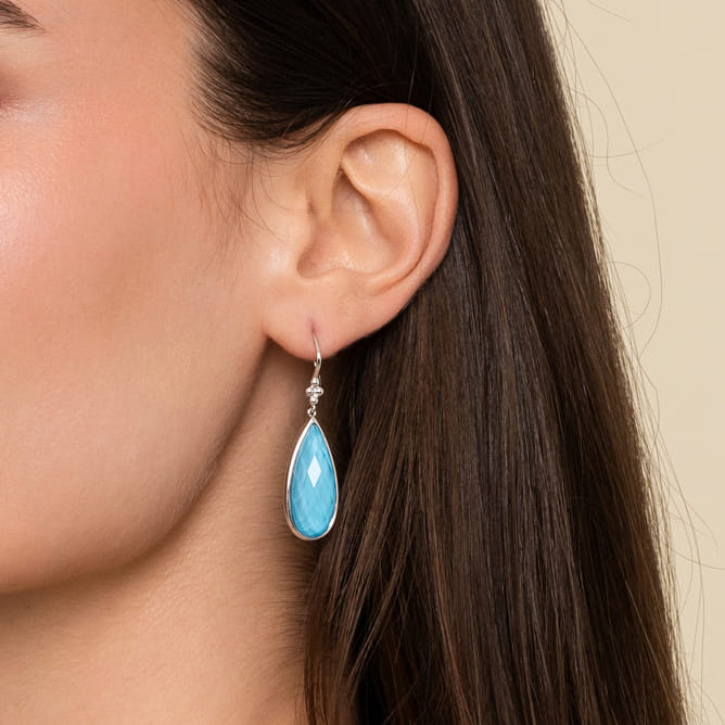 Close-up of a woman's ear wearing a turquoise teardrop earring with a beige background