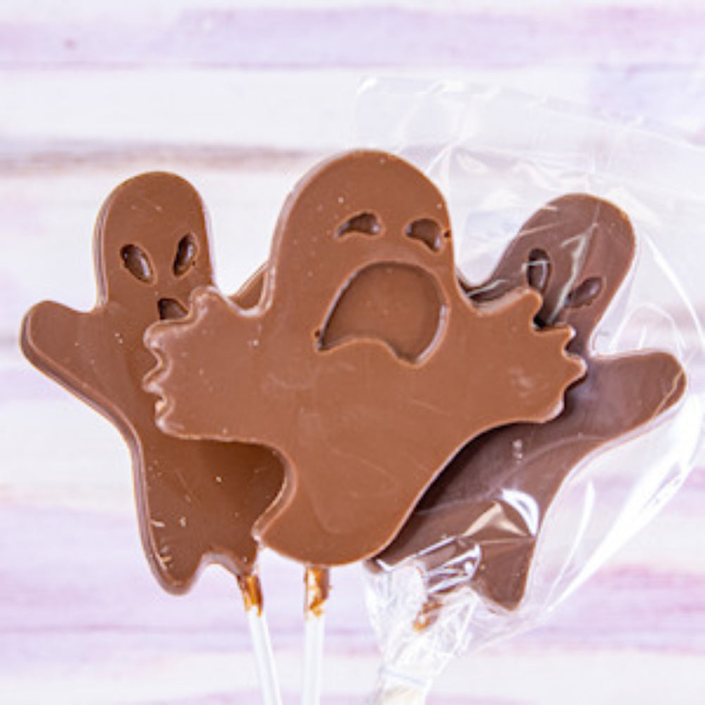 Three ghost-shaped chocolate lollipops in milk brown, wrapped in clear cellophane, on a light pink and white striped background.
