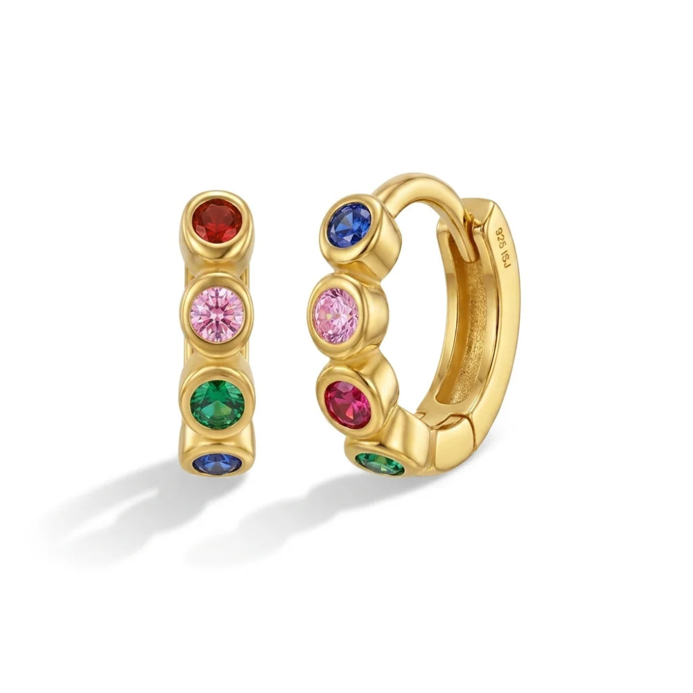 A pair of gold huggie hoop earrings with multiple colorful gemstone accents, shown on a clean white background. One earring is upright, displaying red, pink, green, and blue stones, while the other is angled to show the gold metal and a pink stone.