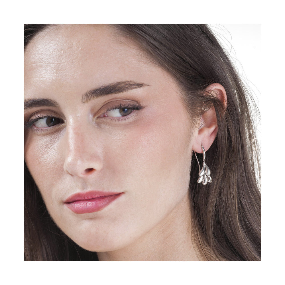 A close-up of a woman wearing a delicate silver dangle earring with a leaf-like design, set against a plain white background.