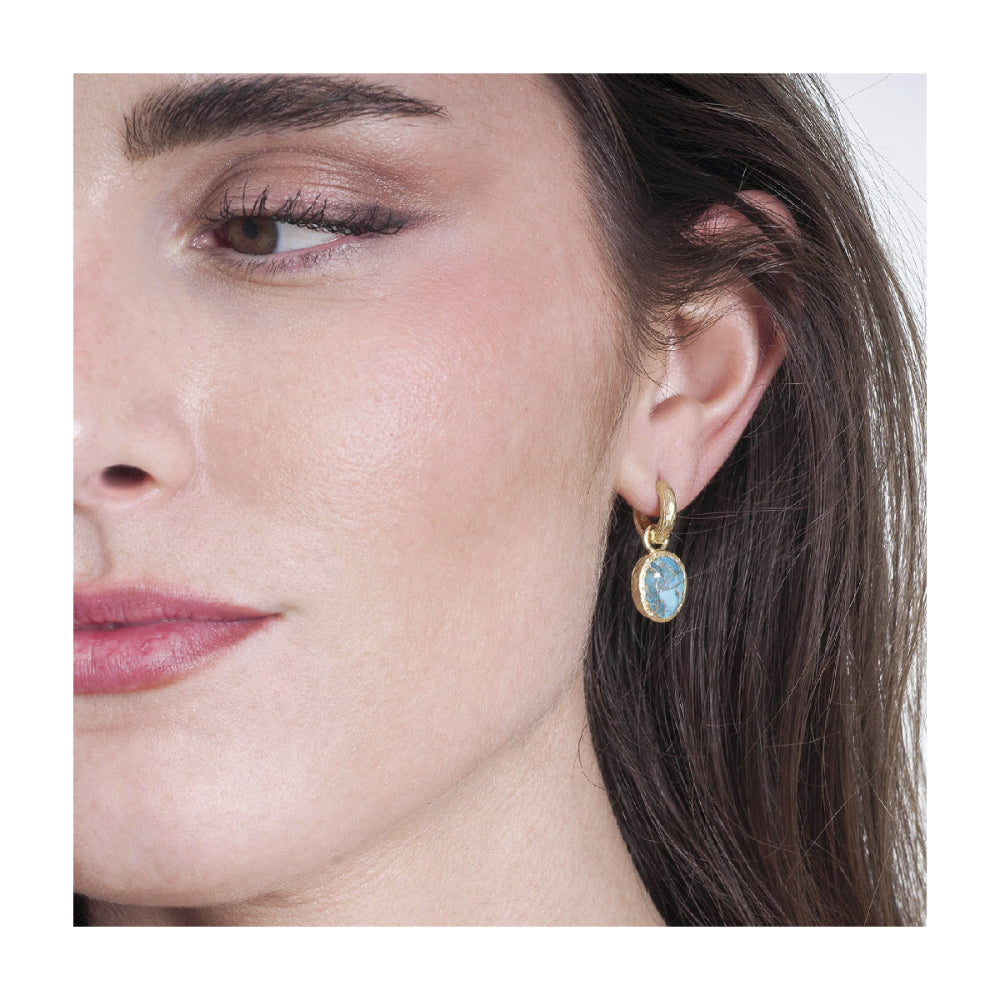 A close-up of a woman's ear wearing a gold hoop earring with an oval light blue stone.