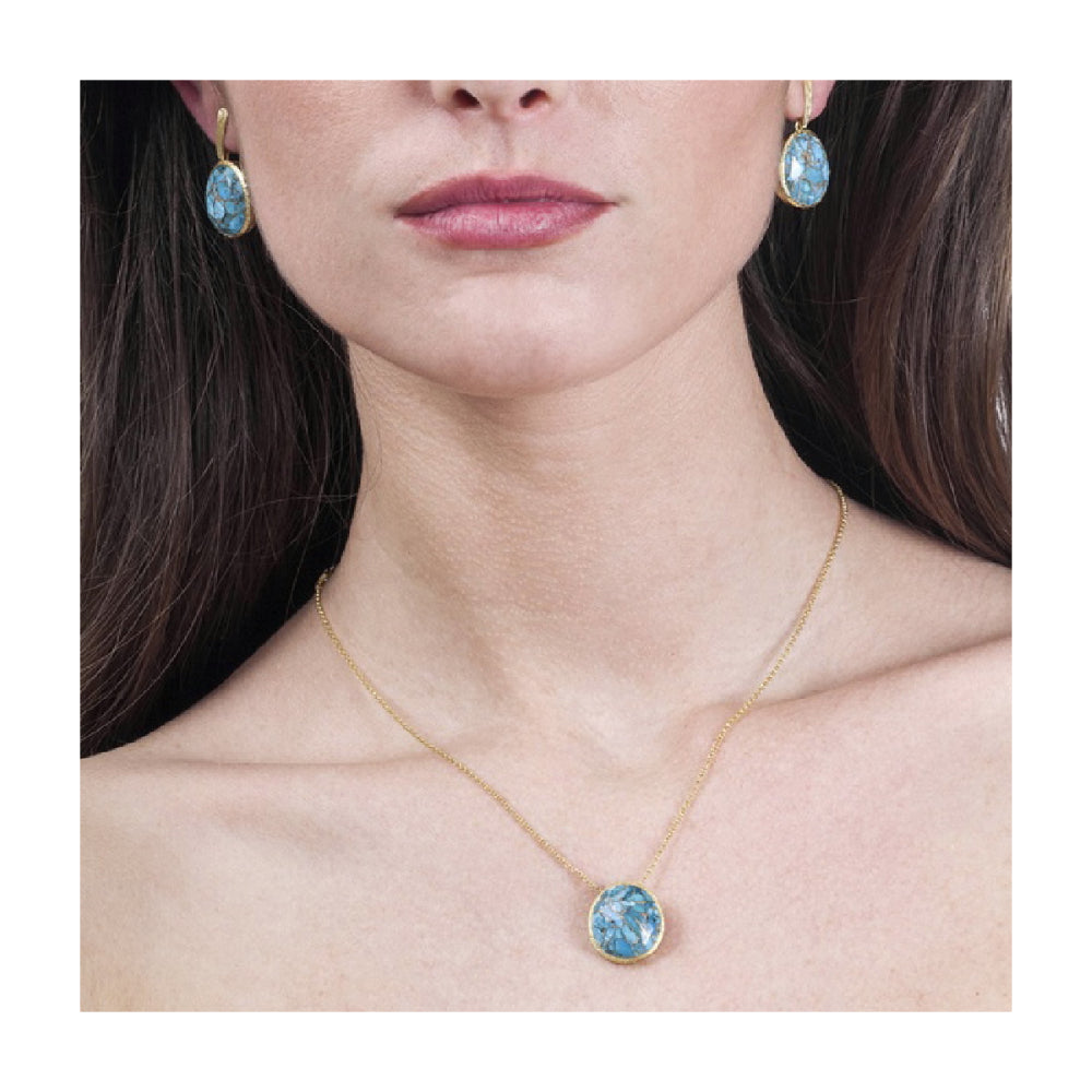 model wearing gold-tone necklace with blue stone center pendant on a natural background. 