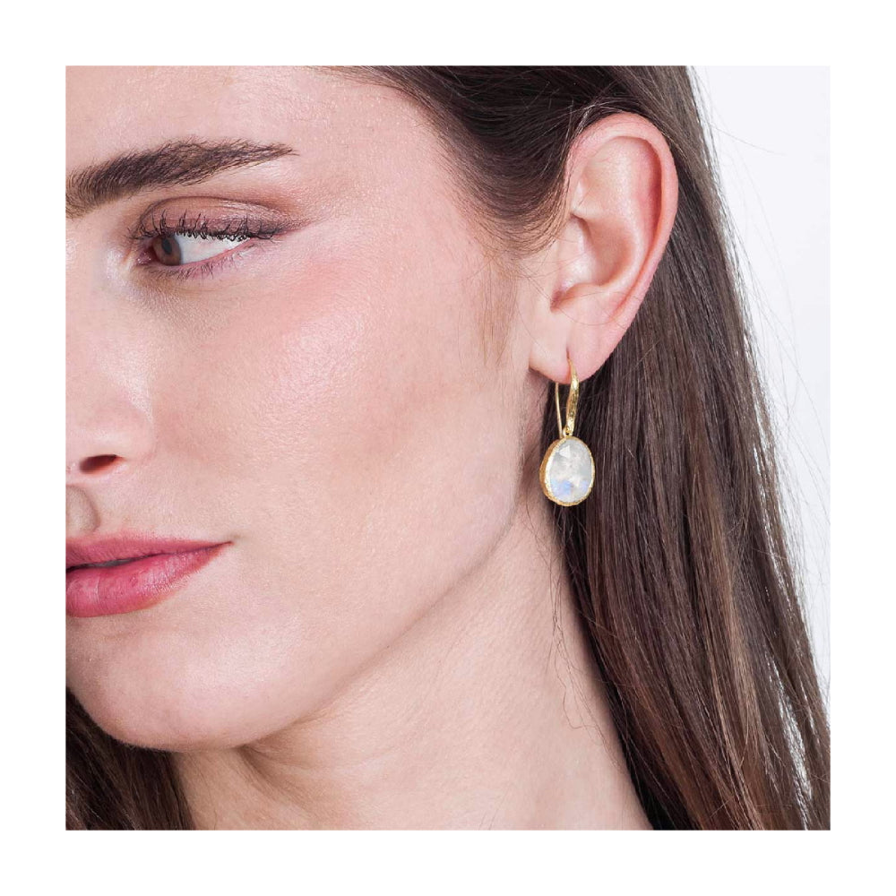 model wearing gold-tone hook earrings with white stones on a natural background