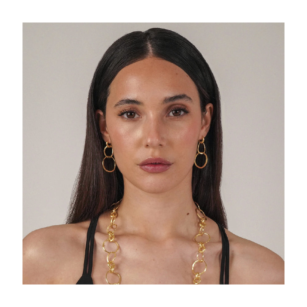 model wearing earrings of three gold rings intertwined on a natural background