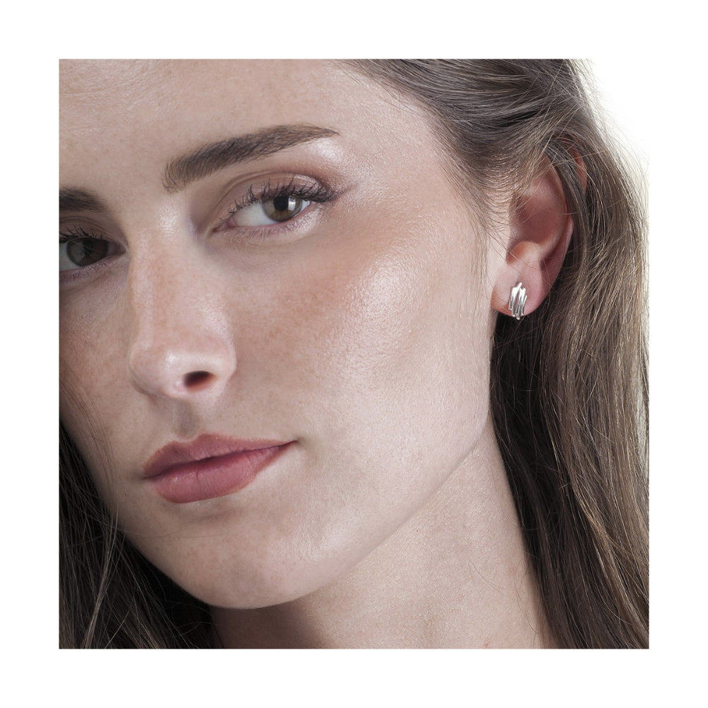 A close-up of a woman's face and ear wearing a small silver stud earring with three clear marquise-cut stones.
