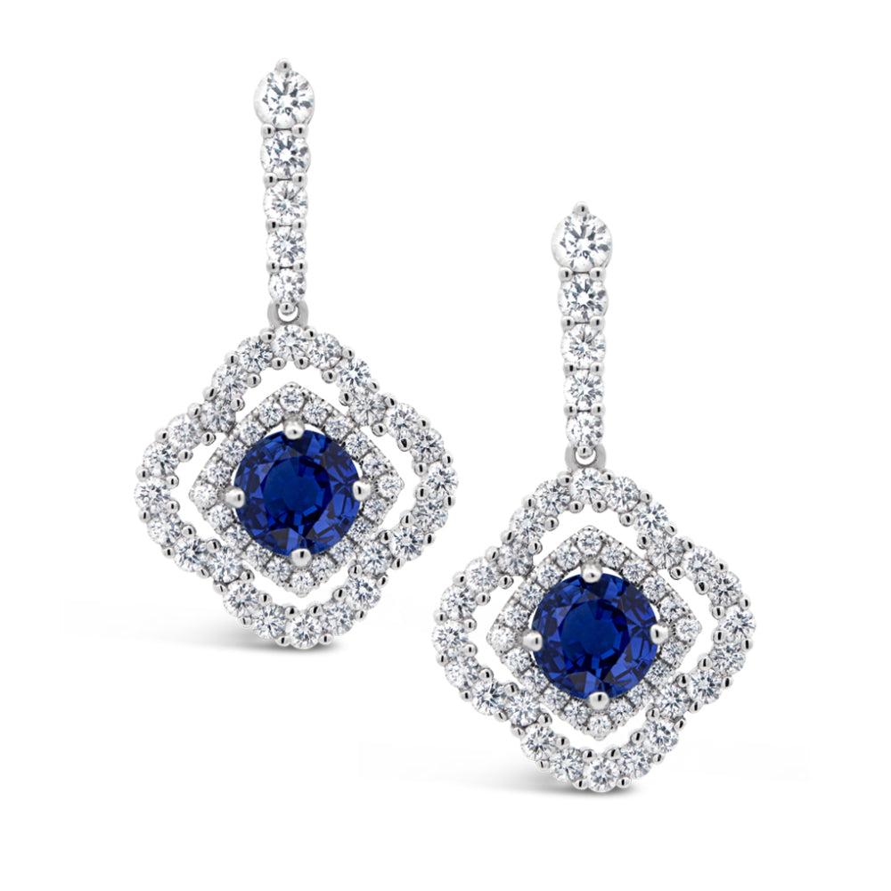 Pair of white gold diamond double halo earrings with blue sapphire centers on a white background