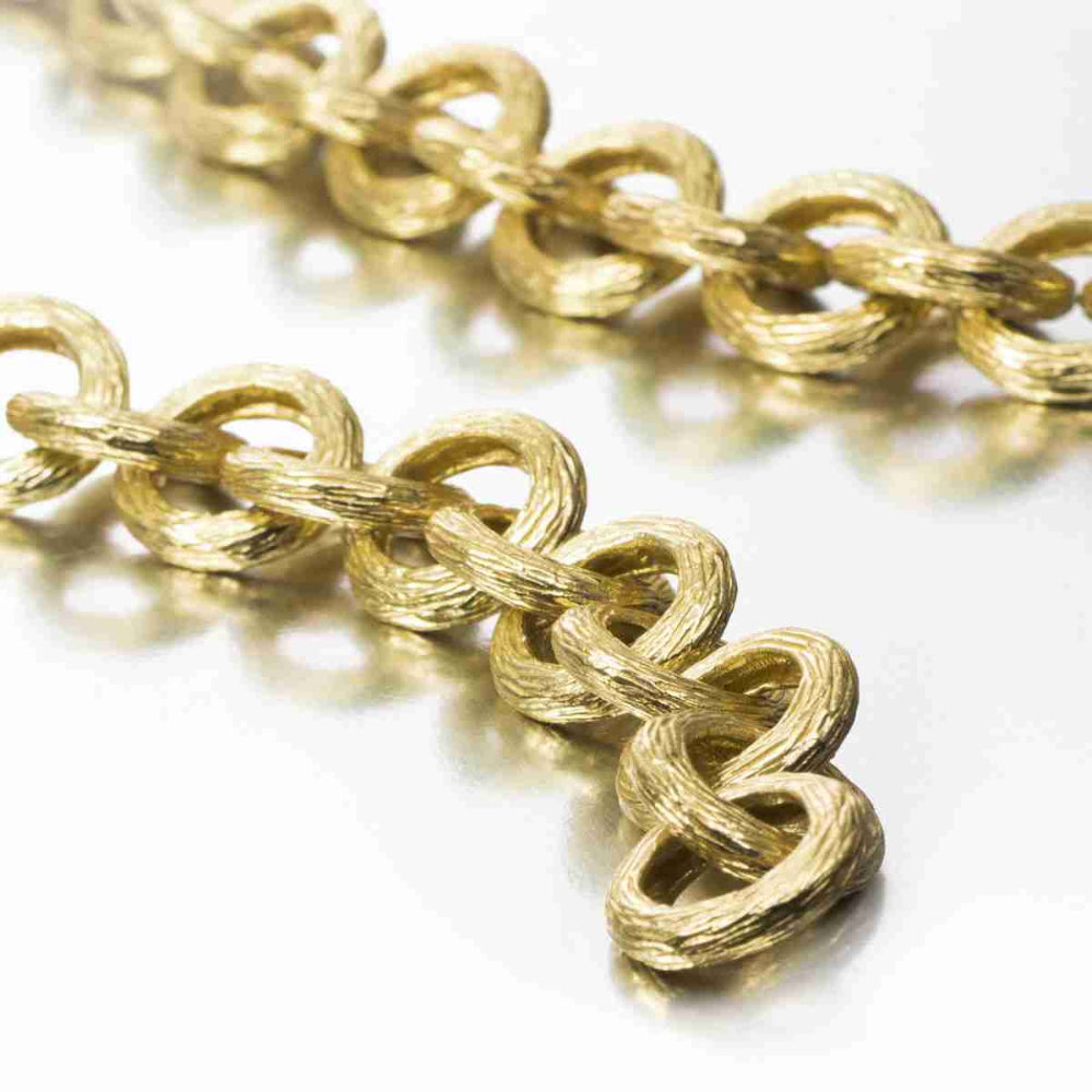 A close-up of a textured gold chain with interlocking oval links on a clean white background.