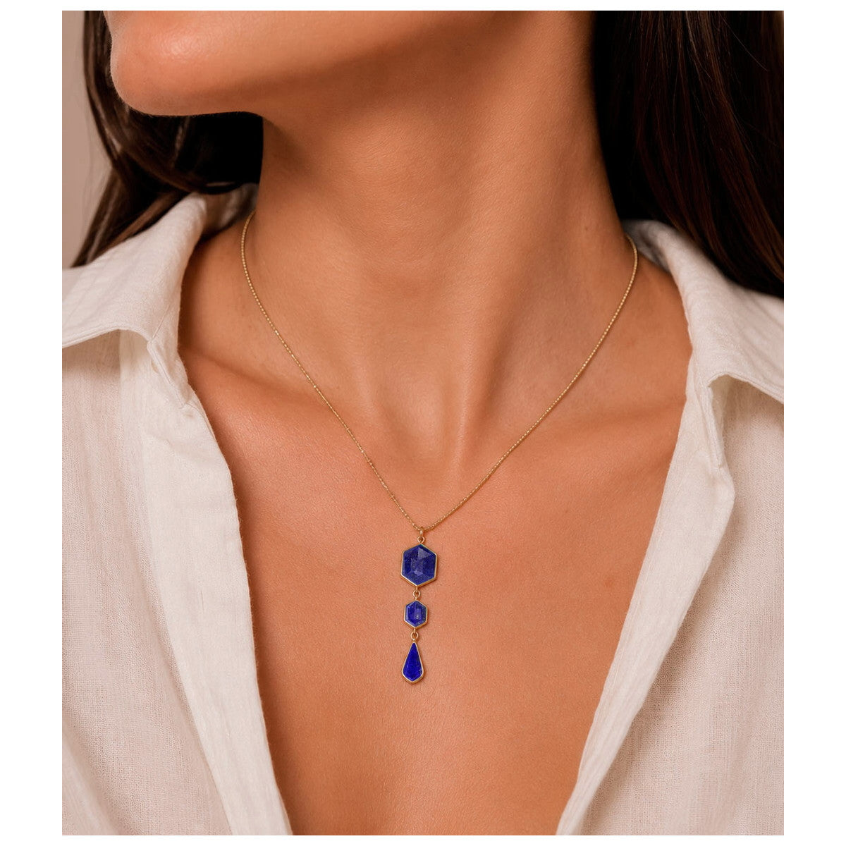 A gold necklace with three stacked blue gemstone pendants, shown worn on a model's neck over a white collared shirt.