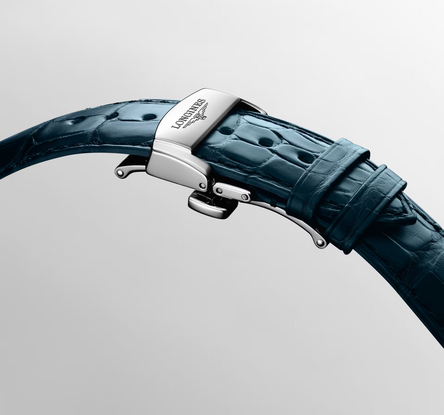 Close-up of a watch strap with a dark teal alligator leather band and a polished silver-toned metal buckle engraved with the Longines logo.