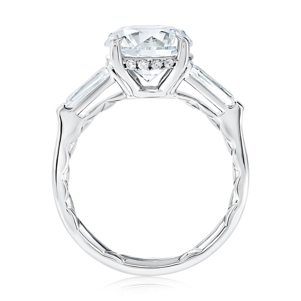 A silver engagement ring featuring a cushion-cut clear center stone and three small round stones in a row beneath the main setting, with baguette-cut side stones on a white background.