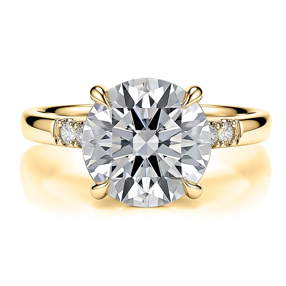 A yellow gold solitaire engagement ring featuring a large round brilliant-cut diamond center stone and small round diamonds on the shoulders, set against a clean white background with a soft reflection.