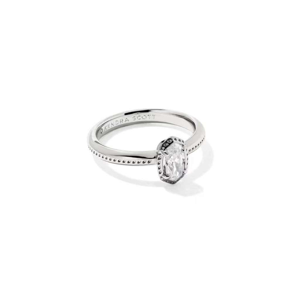 A silver engagement ring featuring an emerald-cut clear center stone in a bezel setting, with a polished band engraved with 'KENDRA SCOTT'.