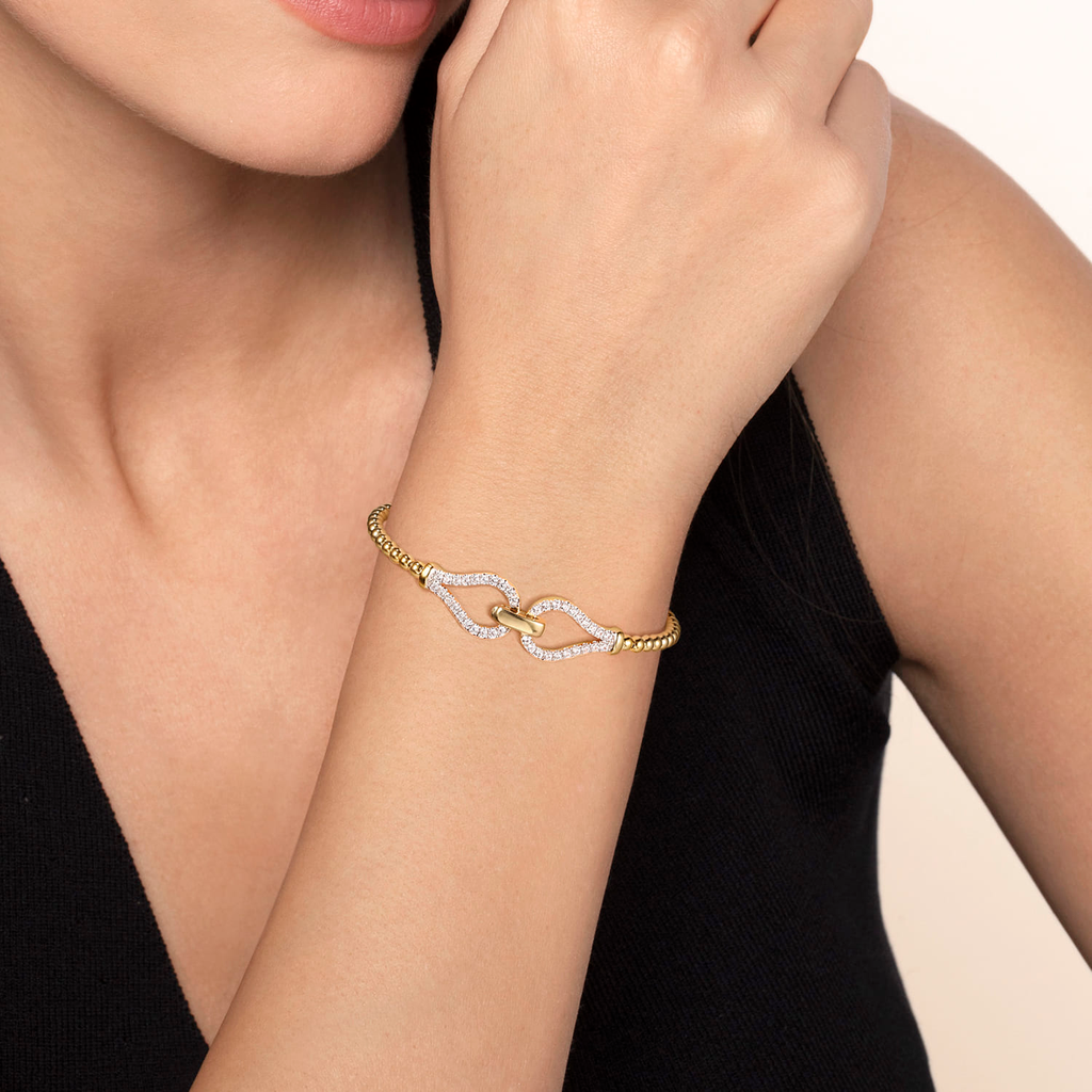 model wearing gold beaded stirrup bangle bracelet with clear stones on natural background