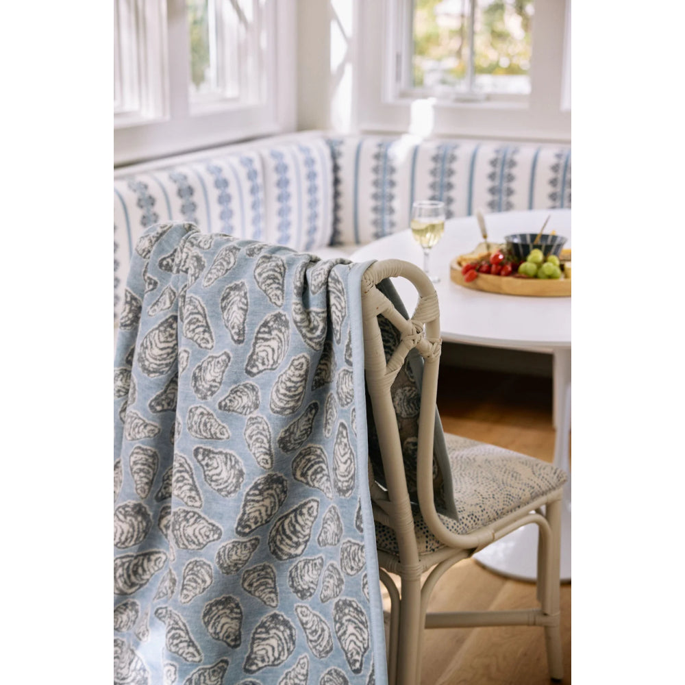 Blue patterned blanket draped over a chair in a bright room with a couch and table in the background.