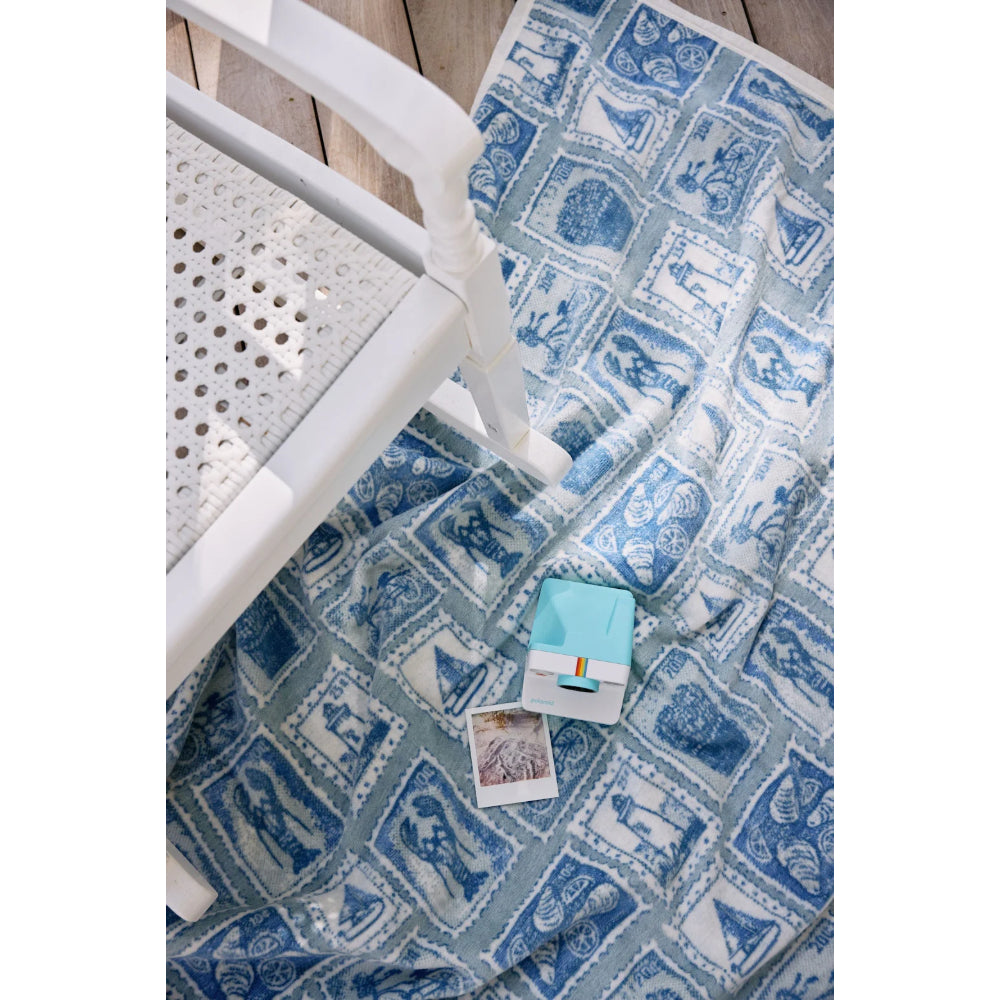 Blue patterned blanket with a white chair and small box on a wooden floor.