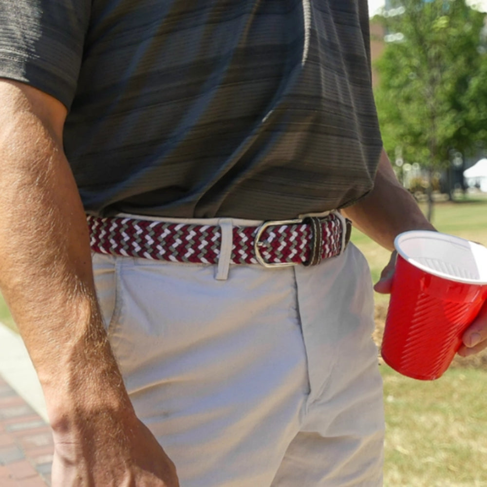 Person holding a red cup with a patterned belt and striped shirt outdoors