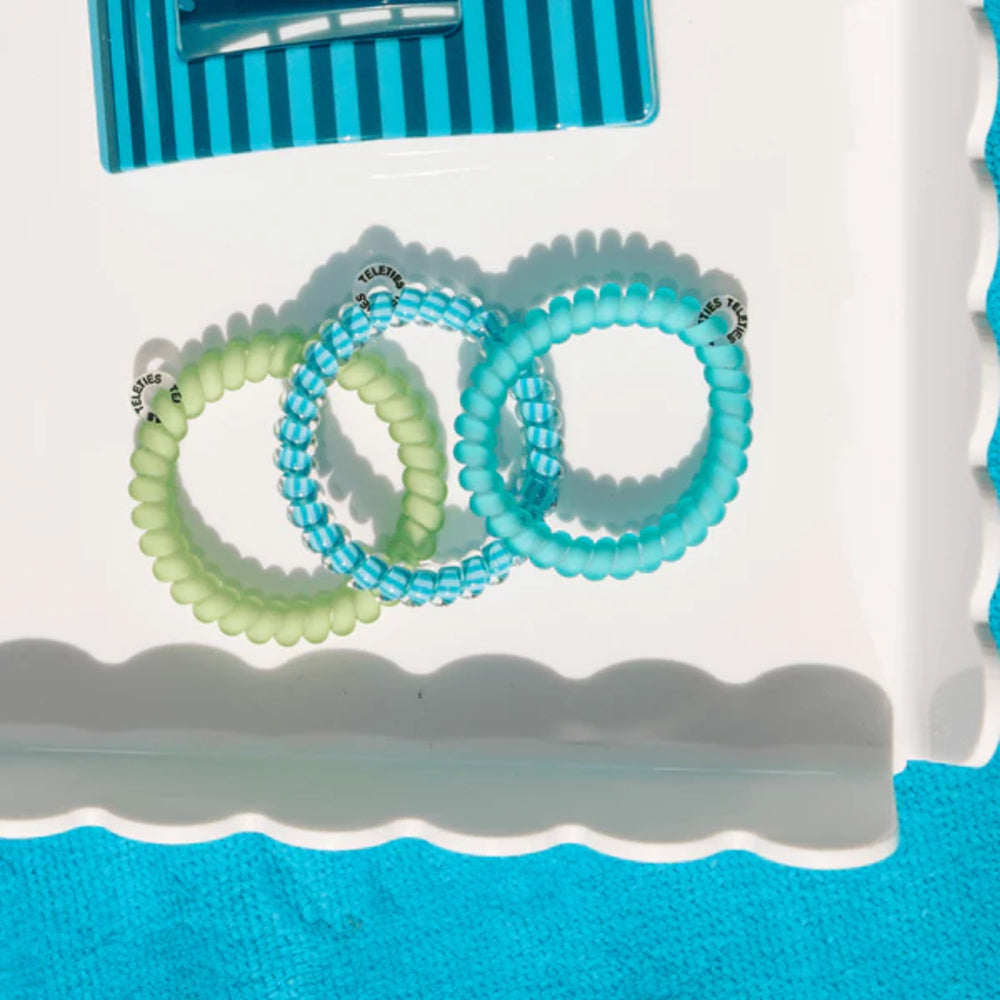Three turquoise beaded hair ties on a white surface with a blue background