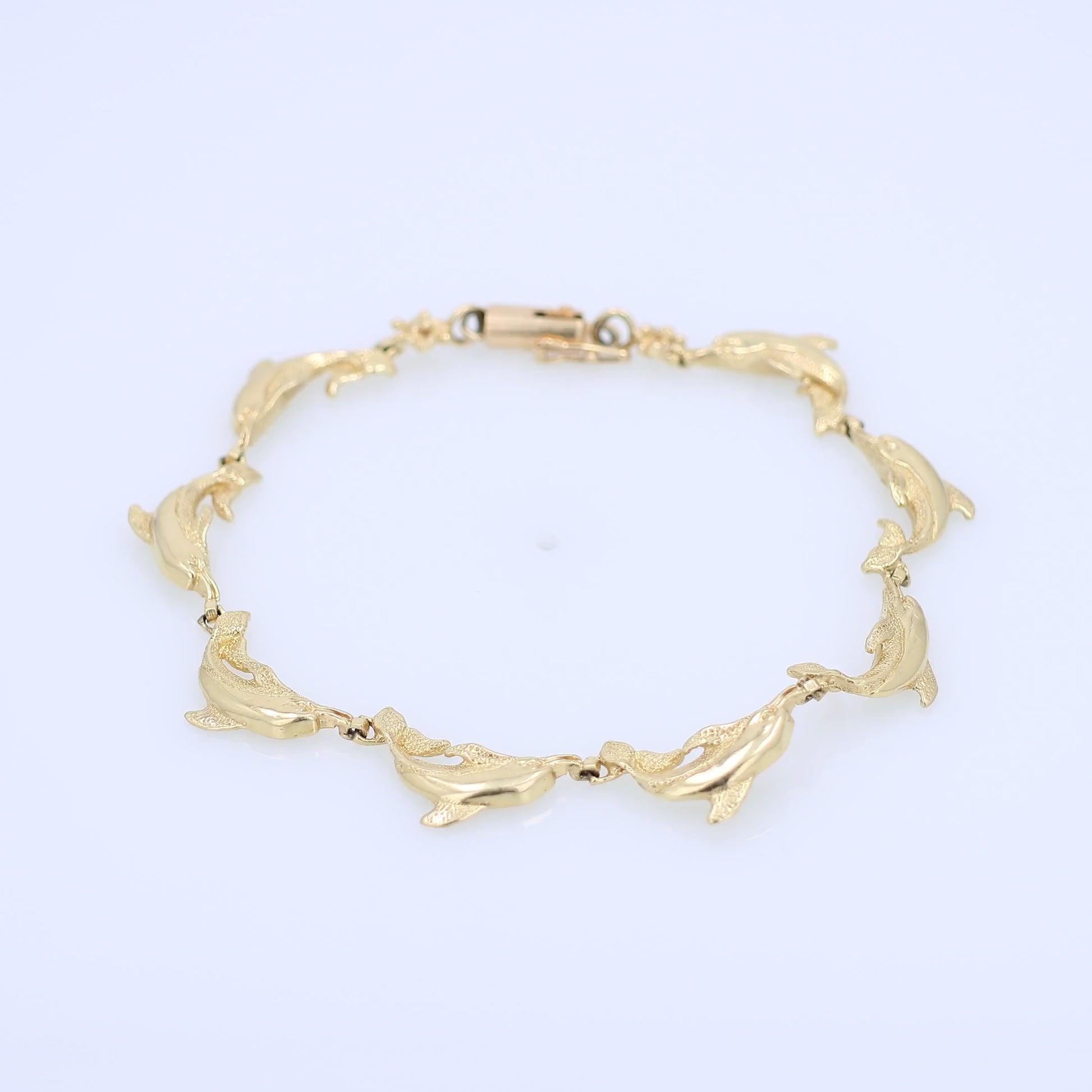 Yellow gold dolphin link bracelet on a white background