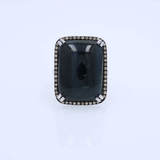 White gold ring with a rectangle cushion cabochon dyed blue cat's eye and a brown single cut diamond halo on a white background