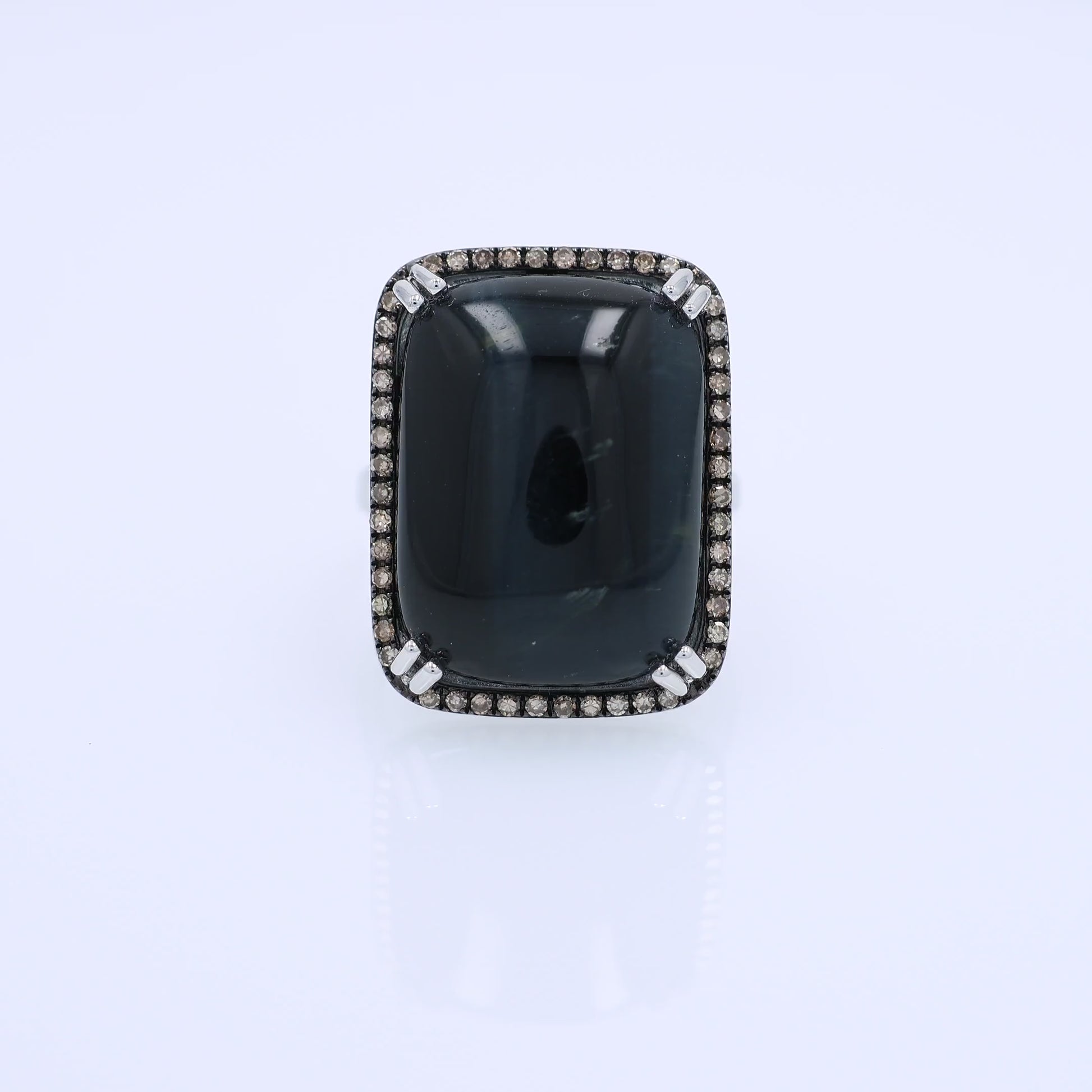 White gold ring with a rectangle cushion cabochon dyed blue cat's eye and a brown single cut diamond halo on a white background