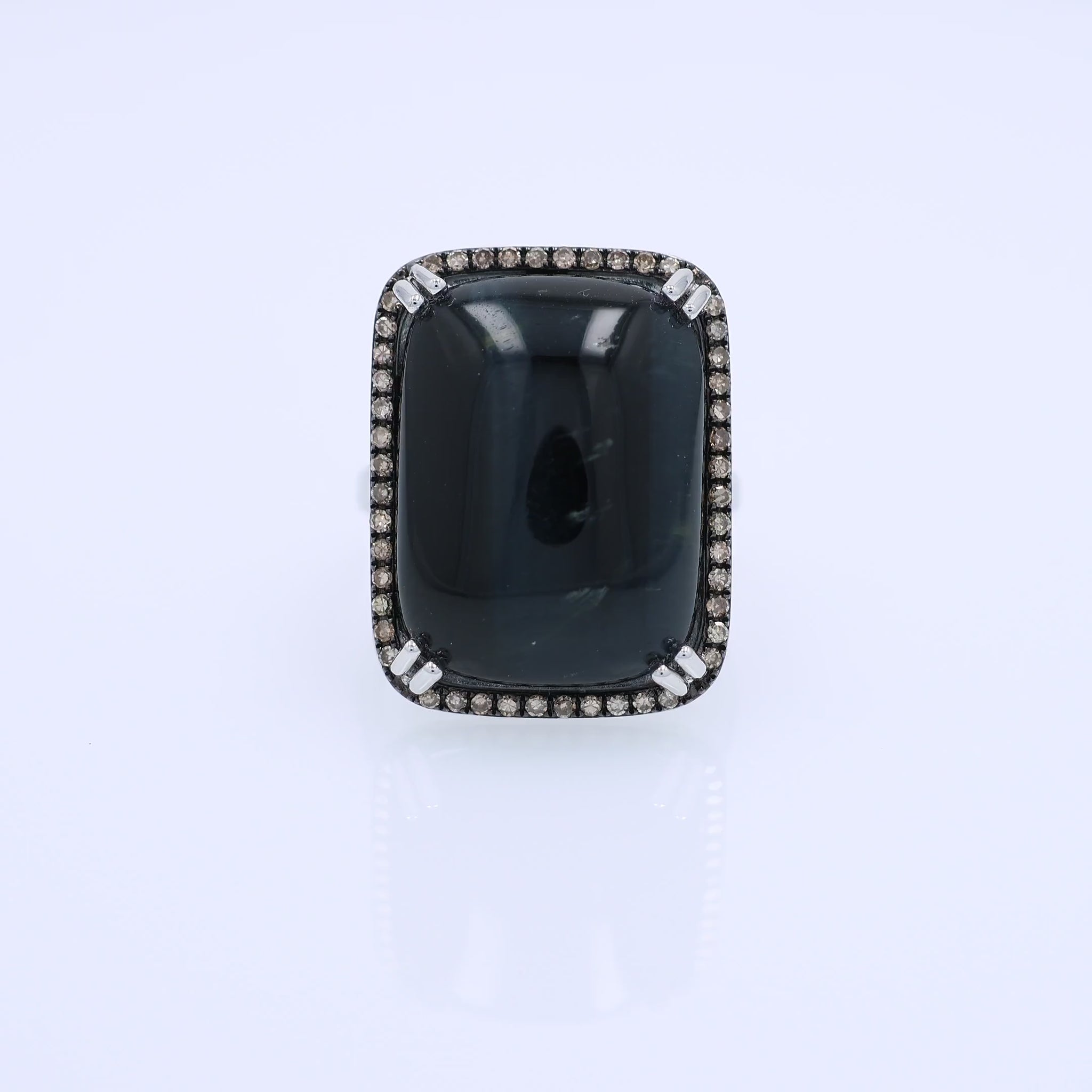 White gold ring with a rectangle cushion cabochon dyed blue cat's eye and a brown single cut diamond halo on a white background