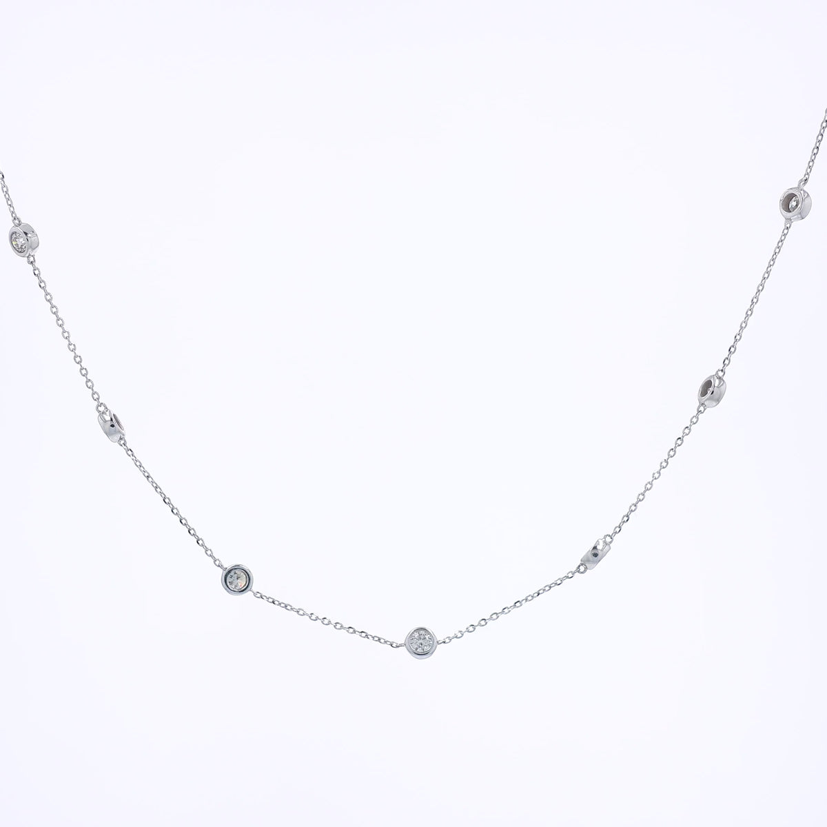 A delicate white gold chain necklace featuring multiple small, bezel-set round diamond stations displayed against a solid white background.