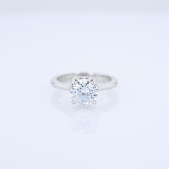 Platinum diamond engagement ring with diamond accents under the head and a round cubic zirconia center on a white background
