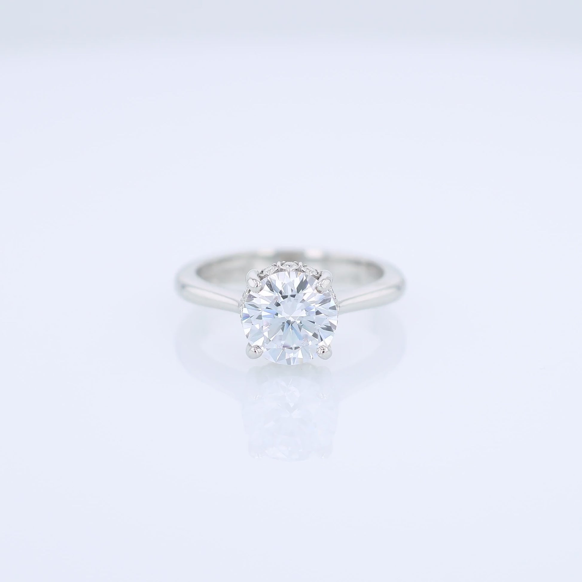 Platinum diamond engagement ring with diamond accents under the head and a round cubic zirconia center on a white background