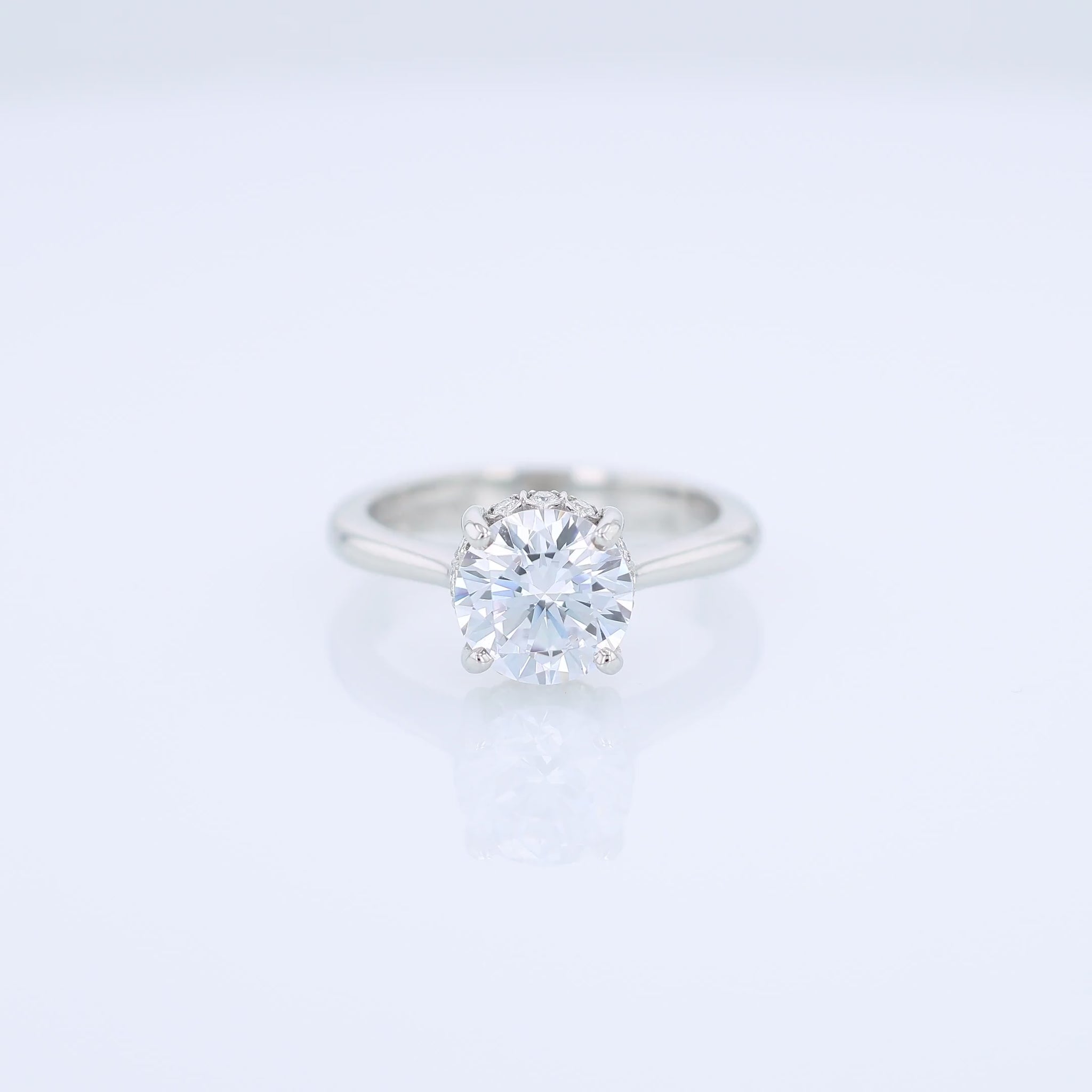 Platinum diamond engagement ring with diamond accents under the head and a round cubic zirconia center on a white background