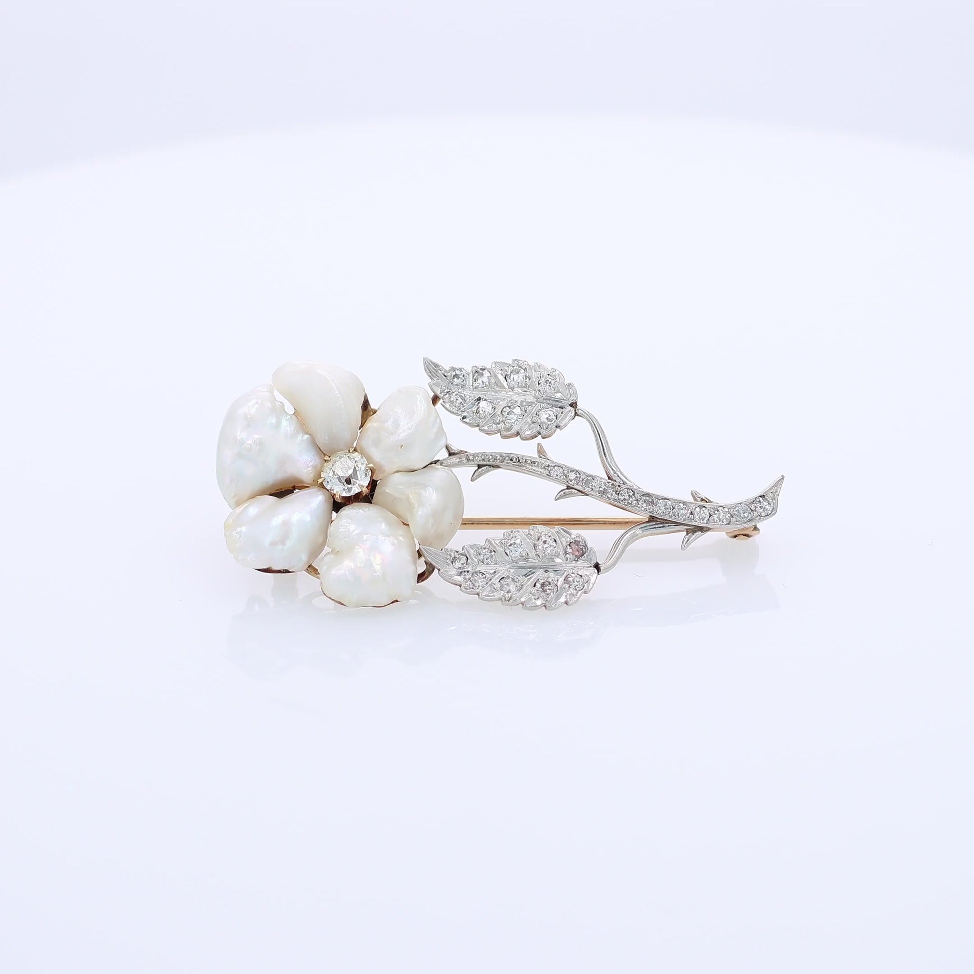Platinum and yellow gold flower design pin with pearl petals and diamond accents on a white background