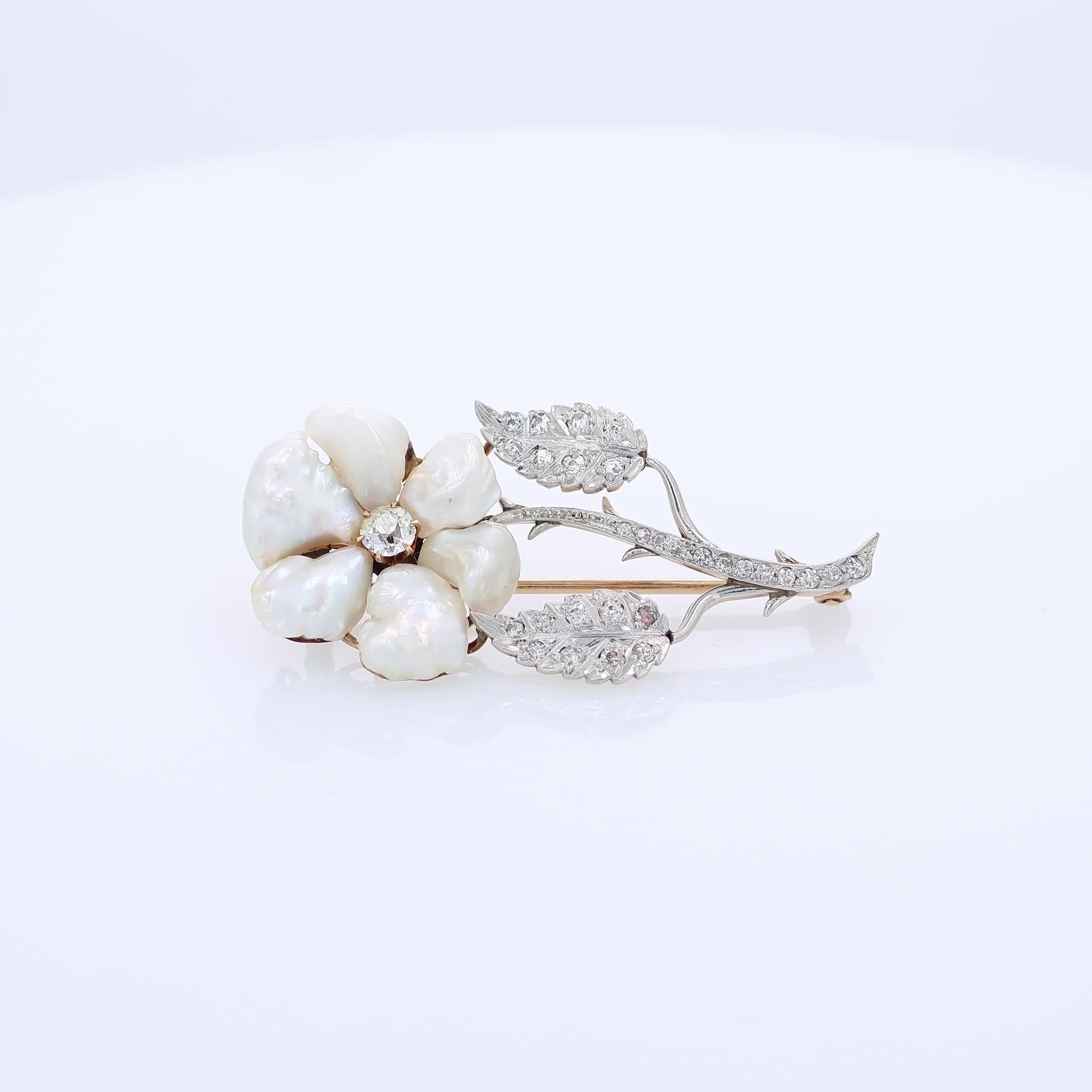 Platinum and yellow gold flower design pin with pearl petals and diamond accents on a white background