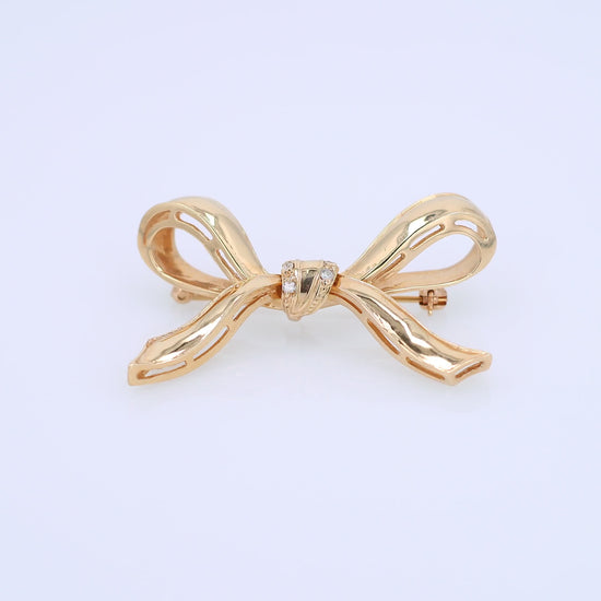 A polished gold bow-shaped brooch with a small cluster of diamonds at the center, shown on a plain white background.