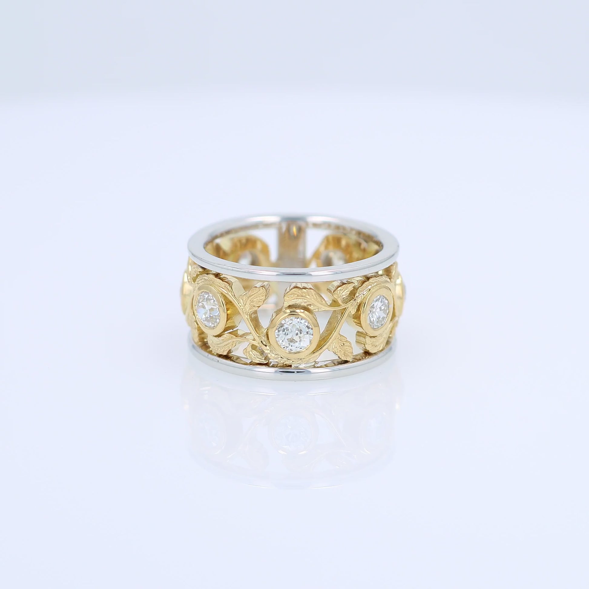 Two-tone gold open work floral band with diamond bezels on a white background