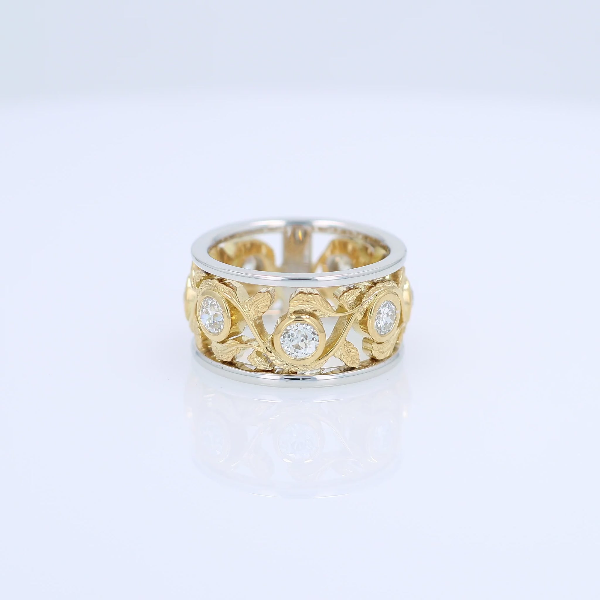 Two-tone gold open work floral band with diamond bezels on a white background