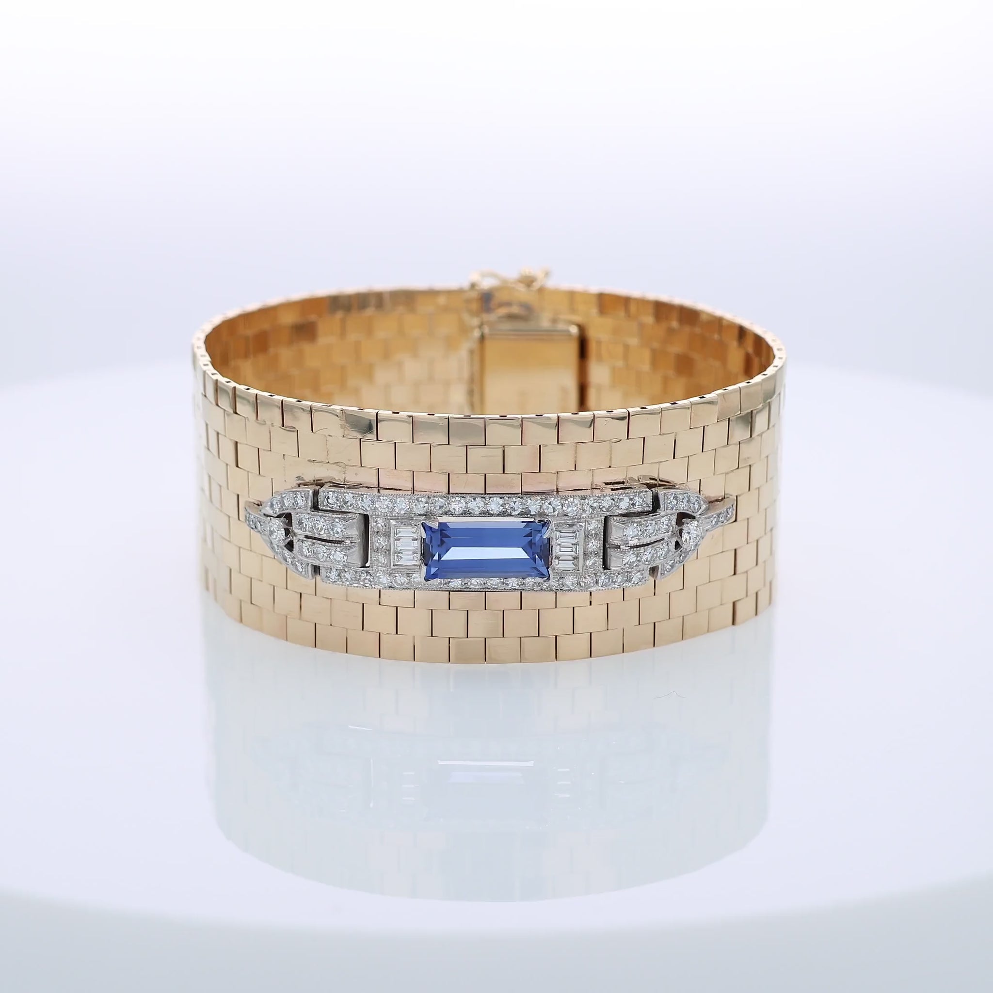 Yellow gold polished wide link design cuff bracelet with a diamond and synthetic sapphire center on a white background