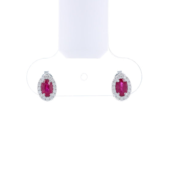 Pair of white gold earrings with oval ruby centers and diamond halos on a white background