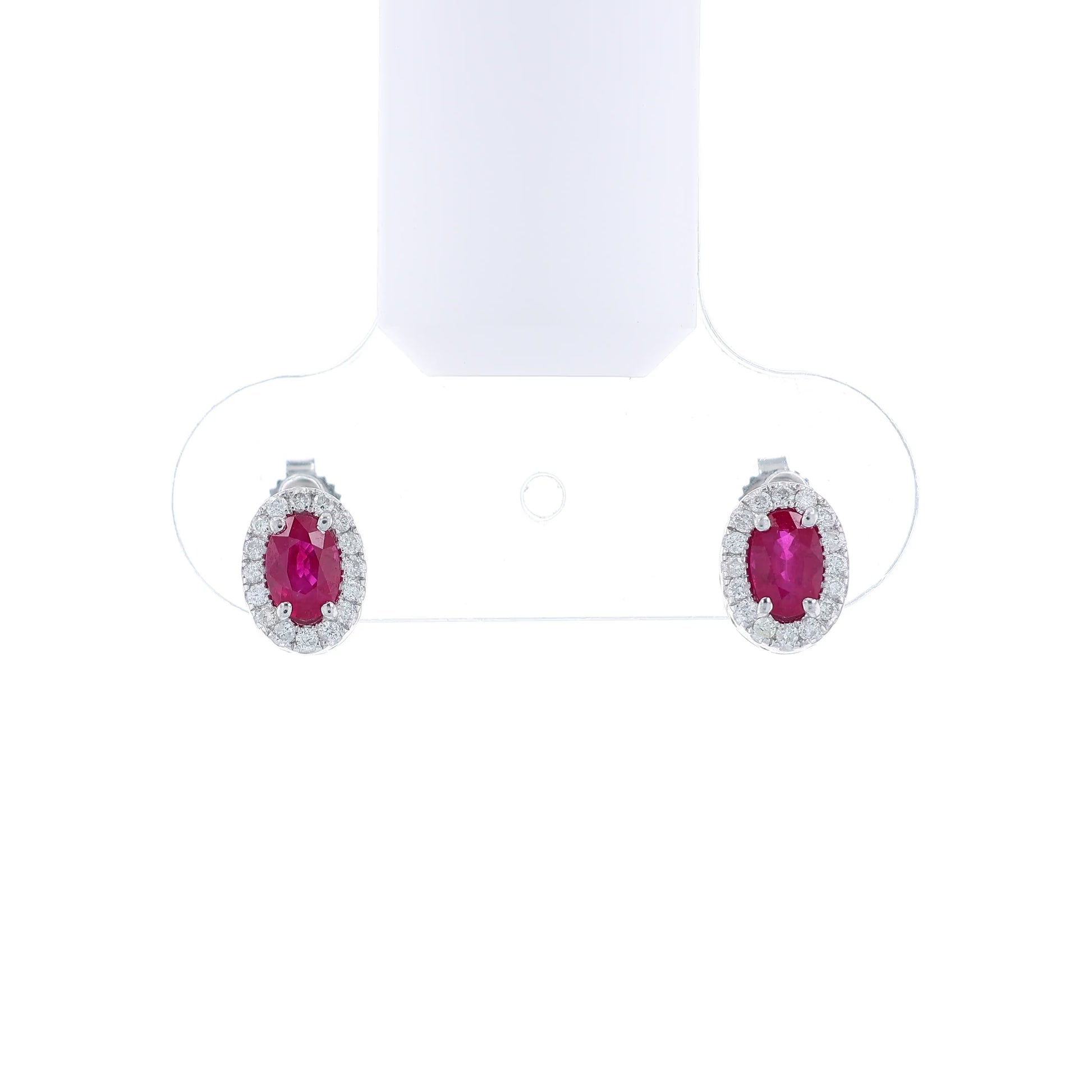 Pair of white gold earrings with oval ruby centers and diamond halos on a white background