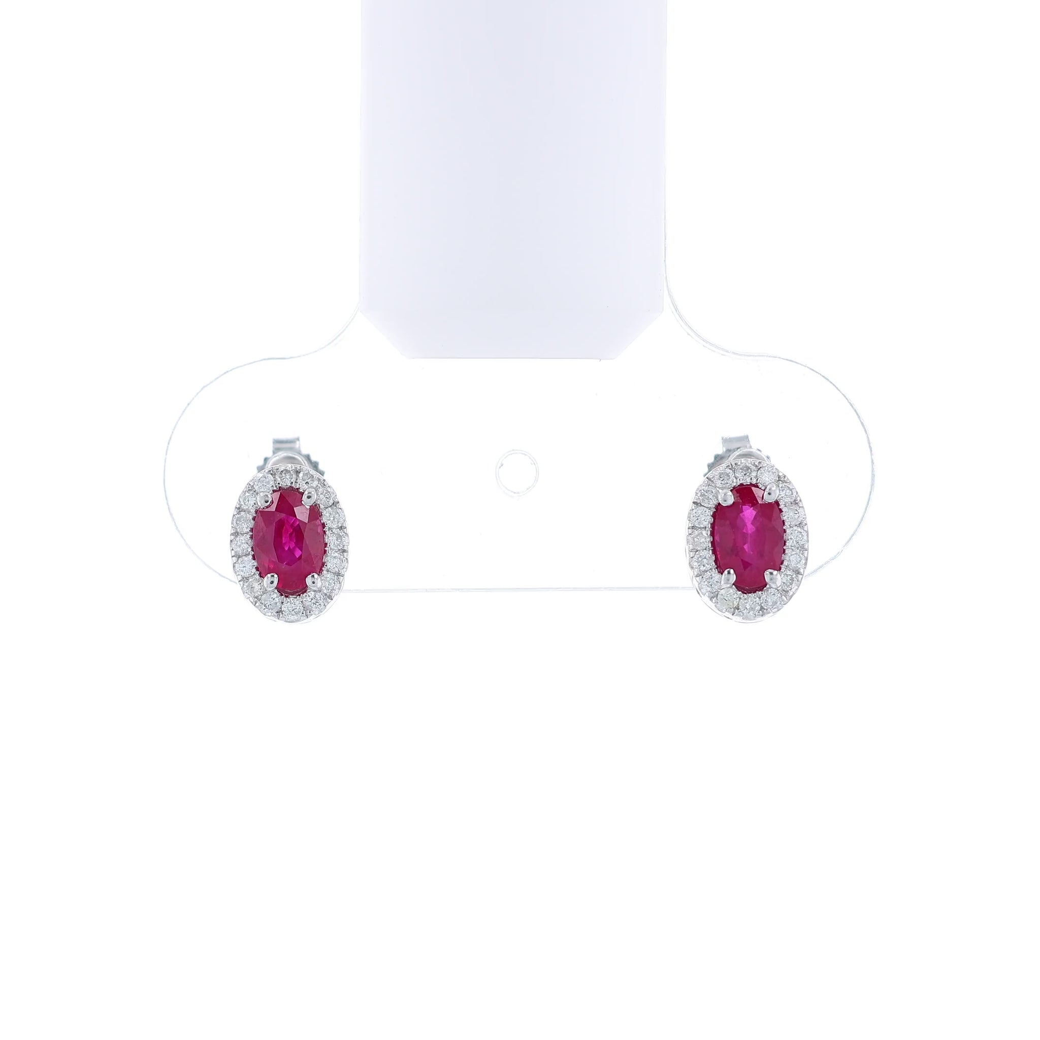 Pair of white gold earrings with oval ruby centers and diamond halos on a white background
