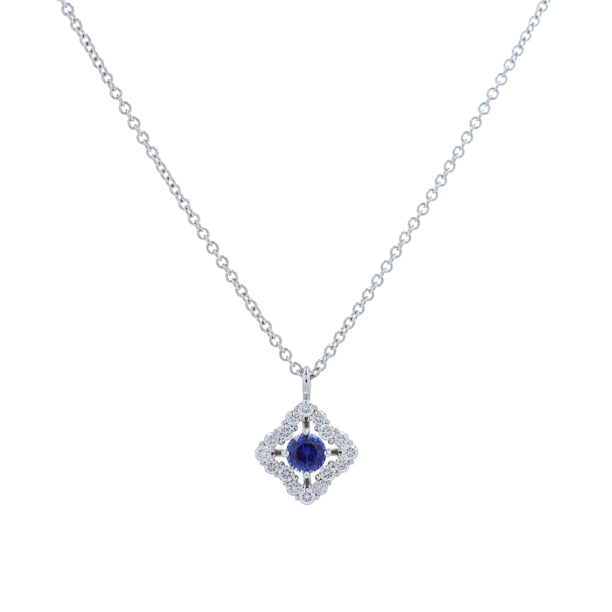 White gold diamond halo pendant necklace with a round blue sapphire center on a white background