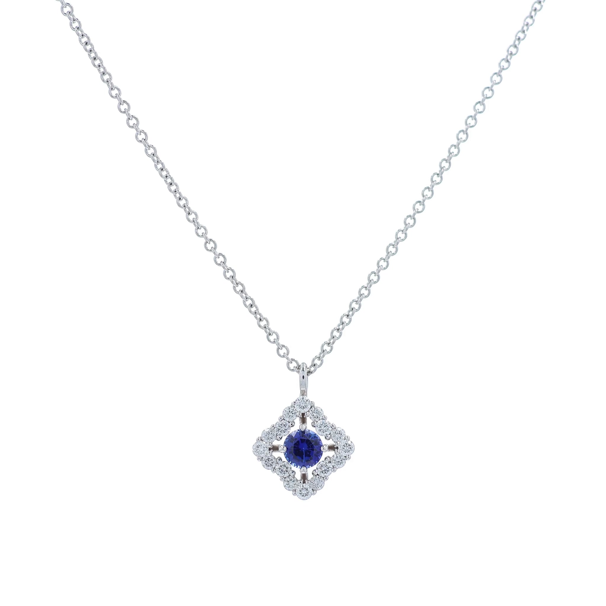 White gold diamond halo pendant necklace with a round blue sapphire center on a white background