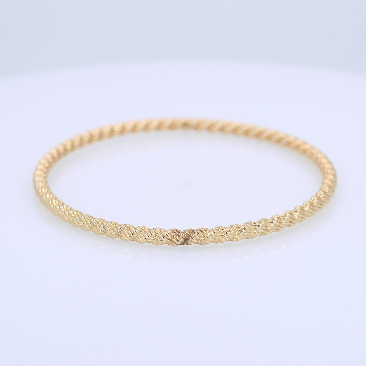 Yellow gold textured twist design 3.8mm slip on bangle bracelet on a white background