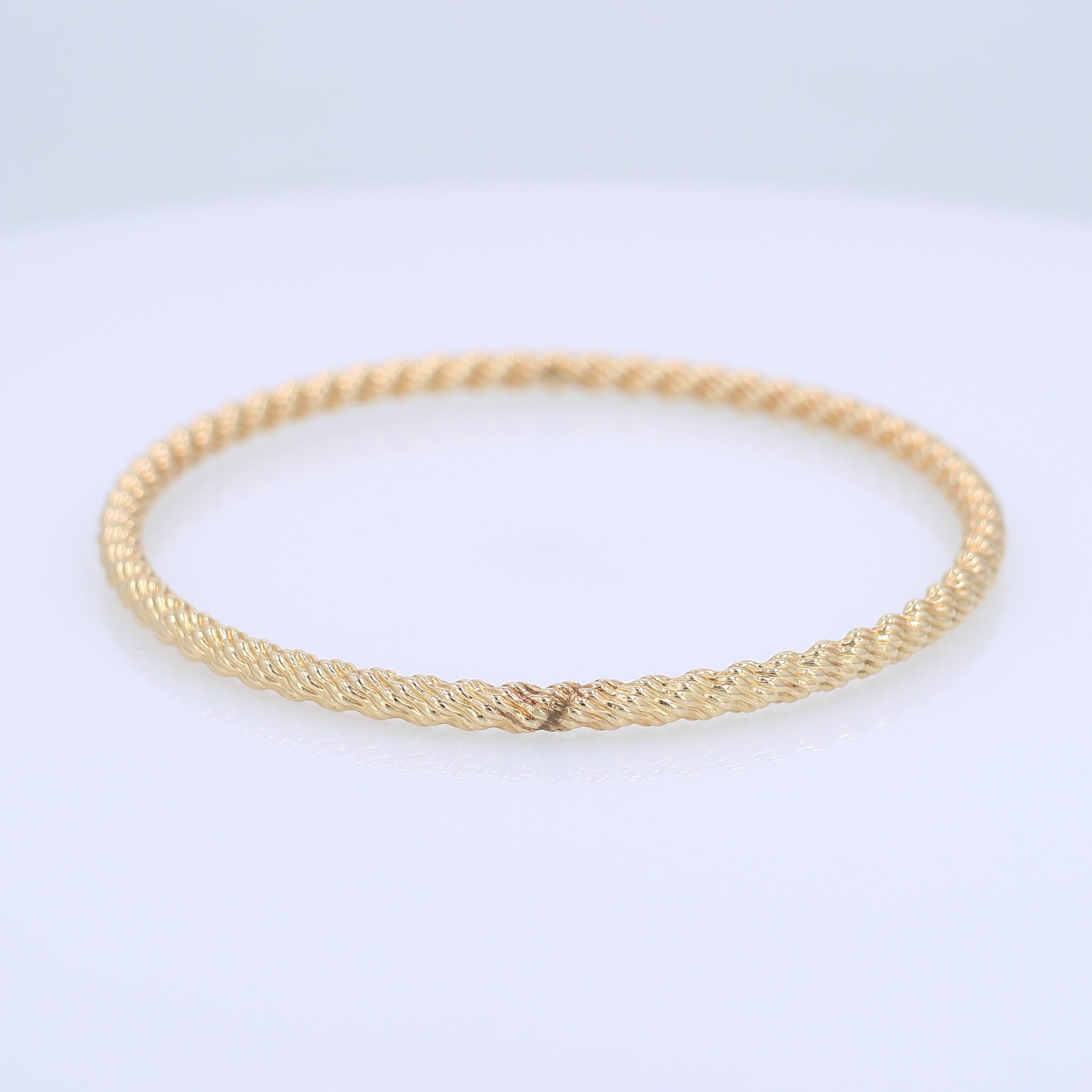 Yellow gold textured twist design 3.8mm slip on bangle bracelet on a white background