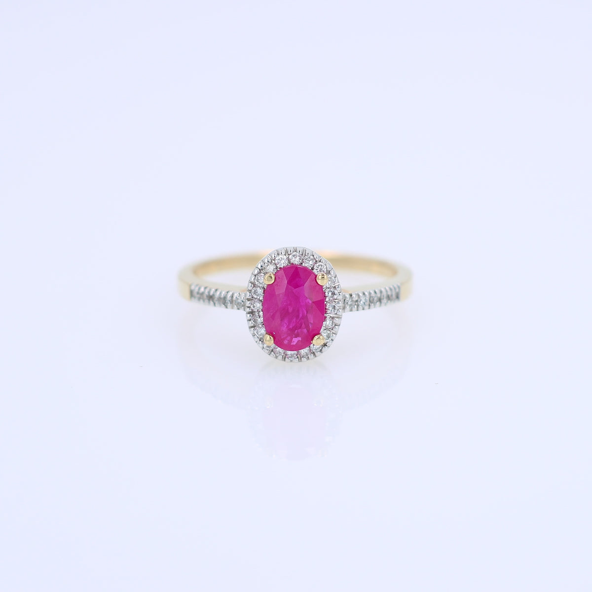 Yellow gold ruby and diamond halo ring on a white background