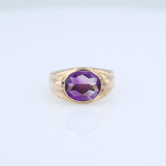 Yellow gold flush bezel set oval amethyst ring on a white background