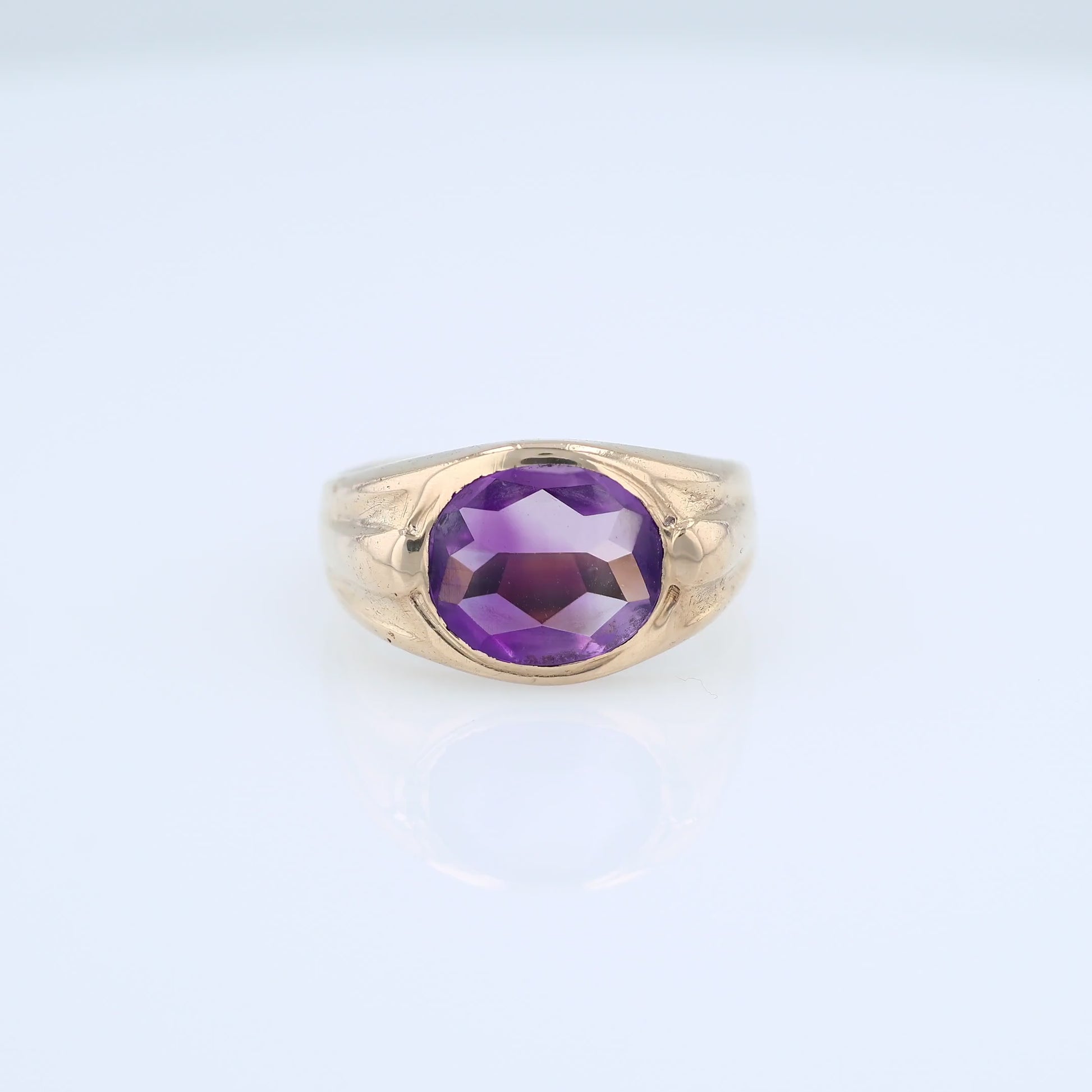 Yellow gold flush bezel set oval amethyst ring on a white background