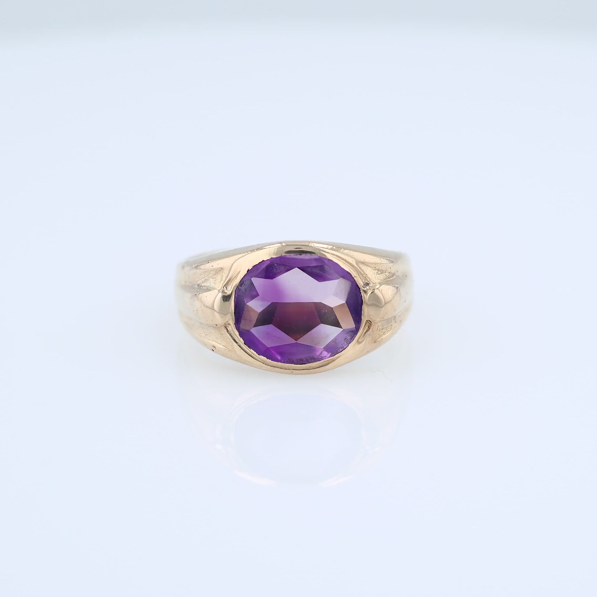 Yellow gold flush bezel set oval amethyst ring on a white background