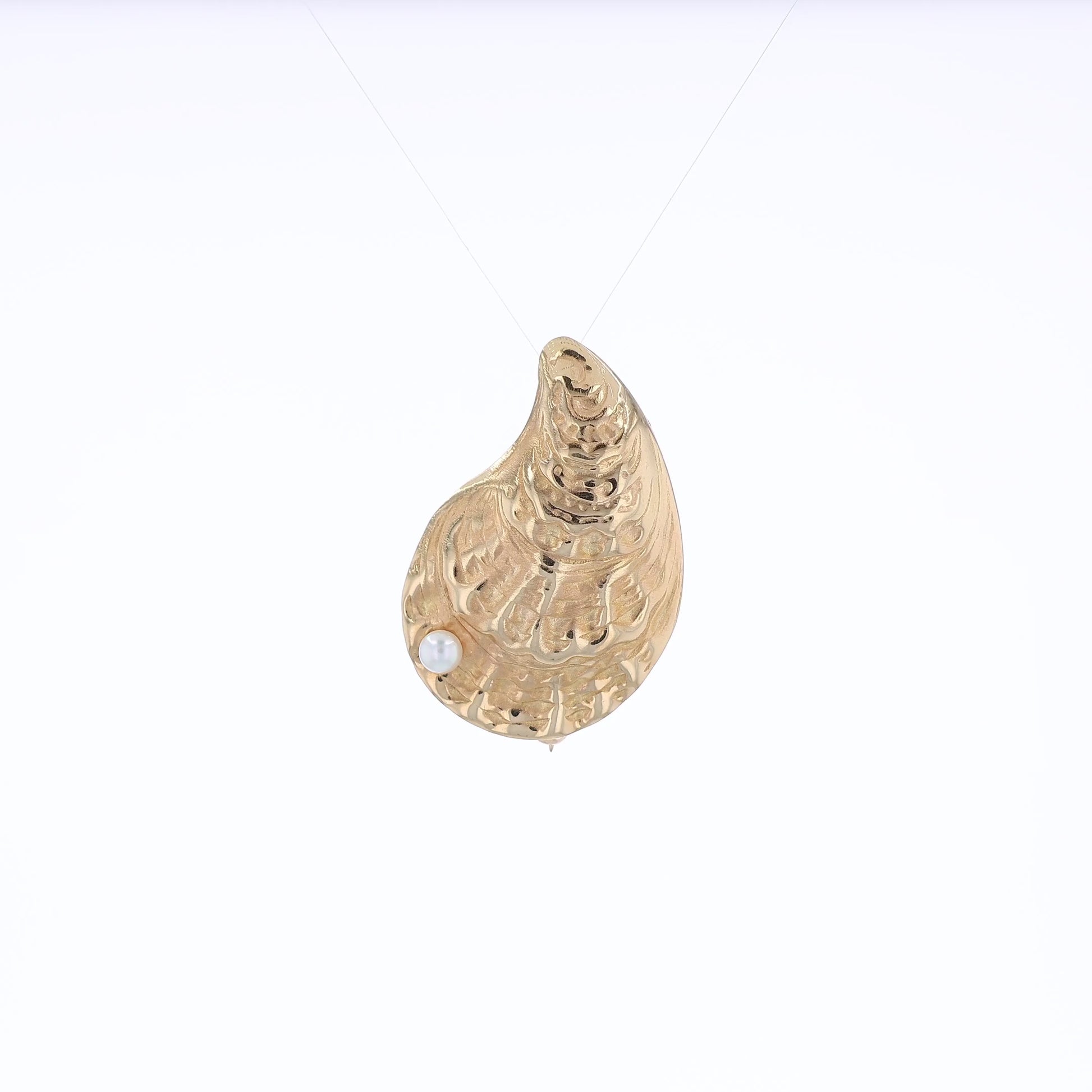 Yellow gold oyster shell pin with a pearl on a white background