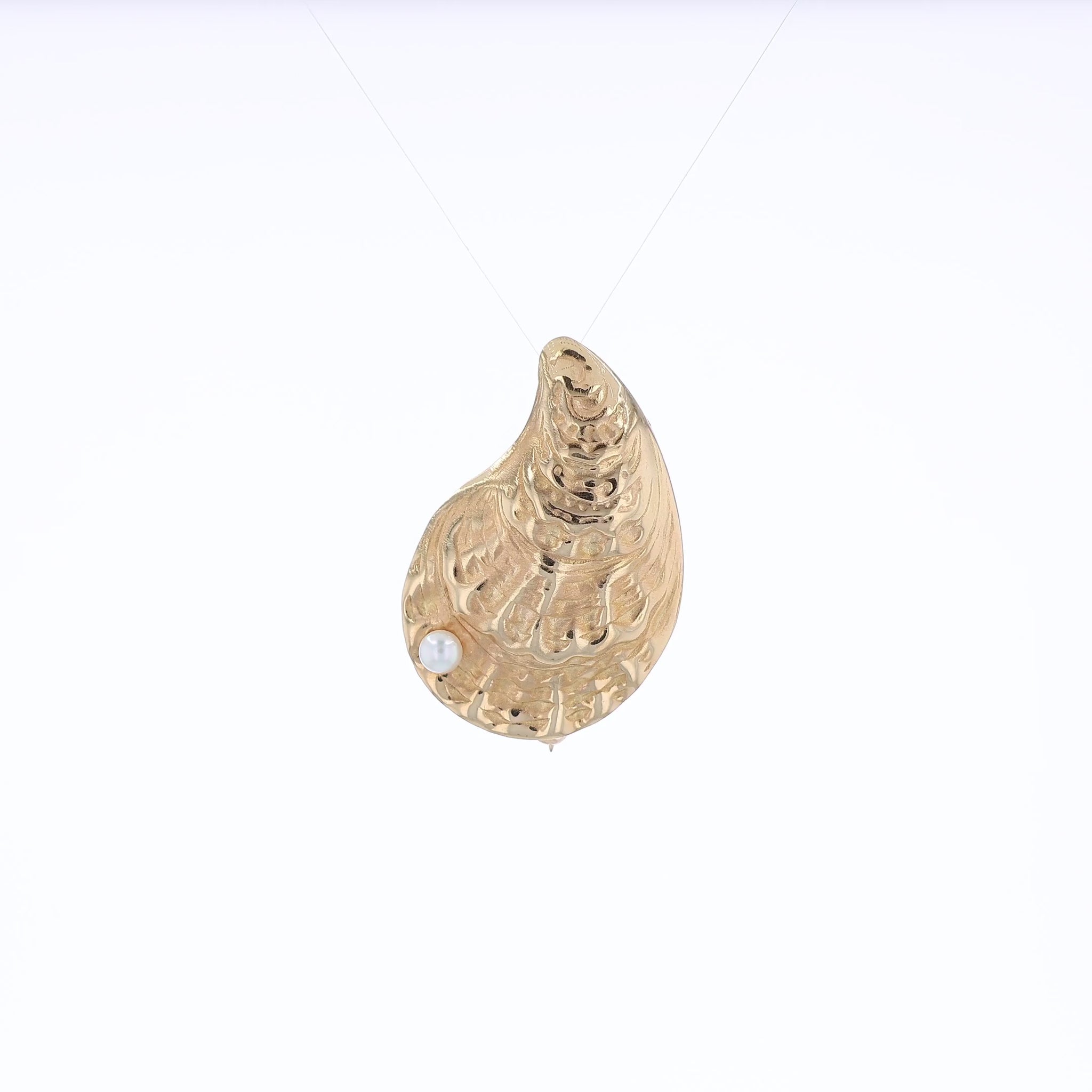 Yellow gold oyster shell pin with a pearl on a white background