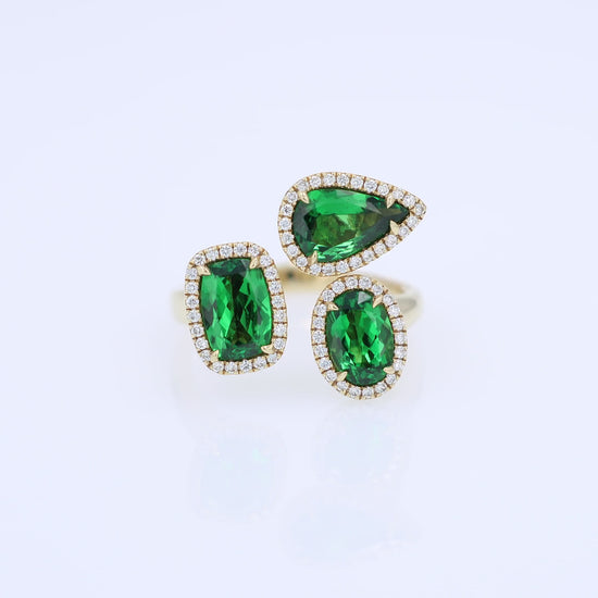 Gold ring with green tsavorite garnets and diamond halos on a white background