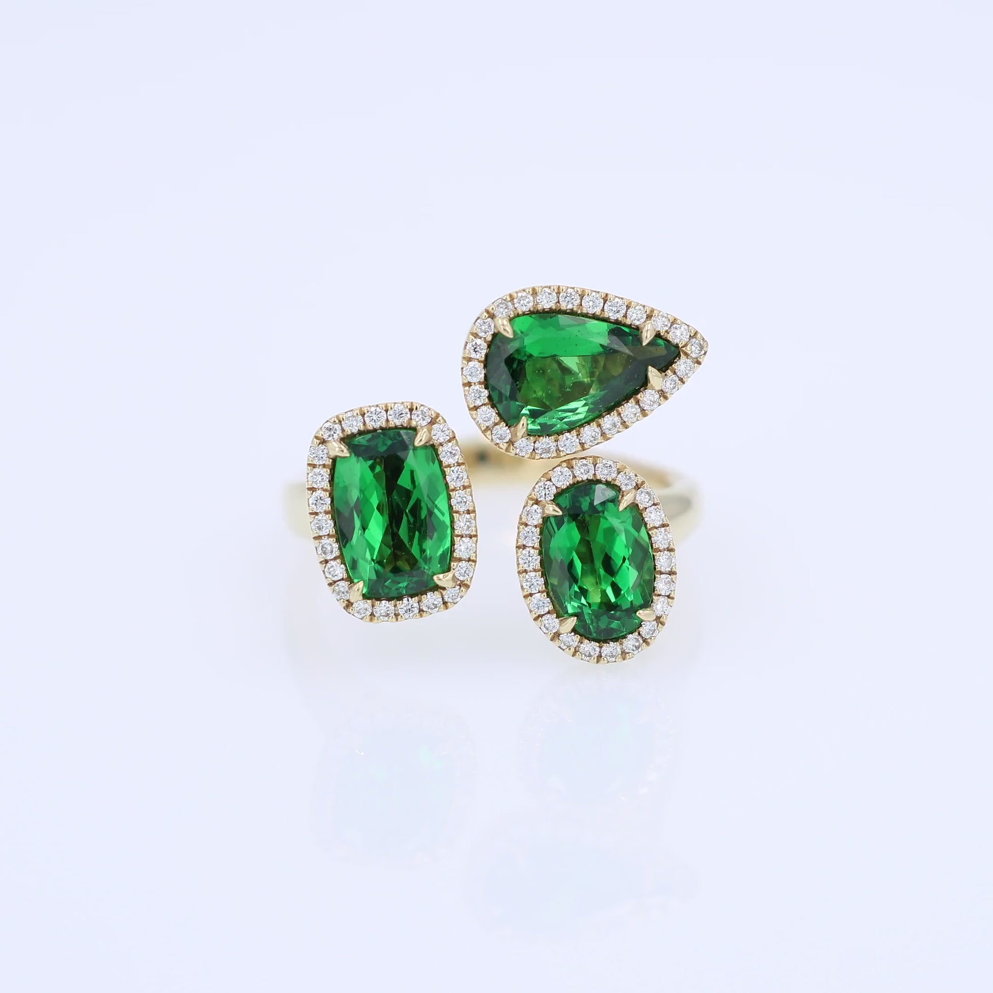 Gold ring with green tsavorite garnets and diamond halos on a white background
